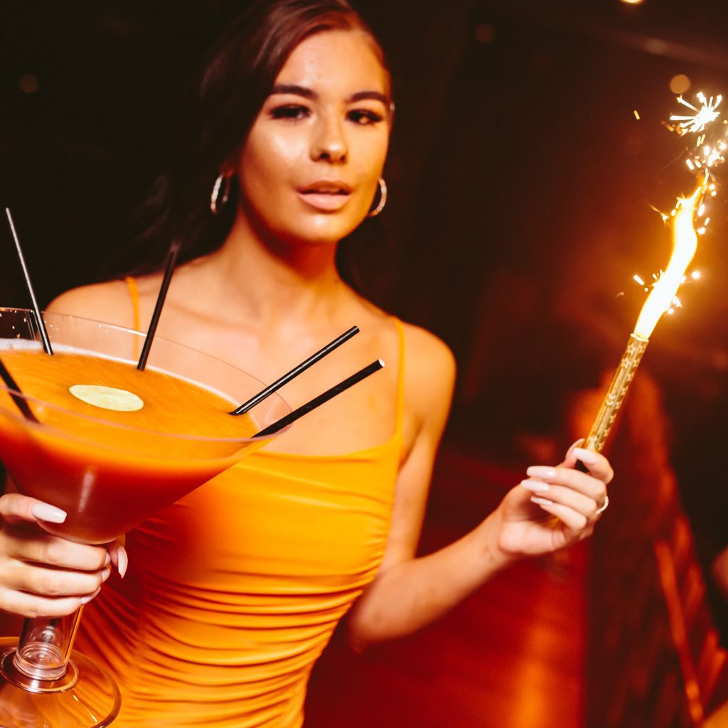 Girl holding a sparkler and big orange cocktail