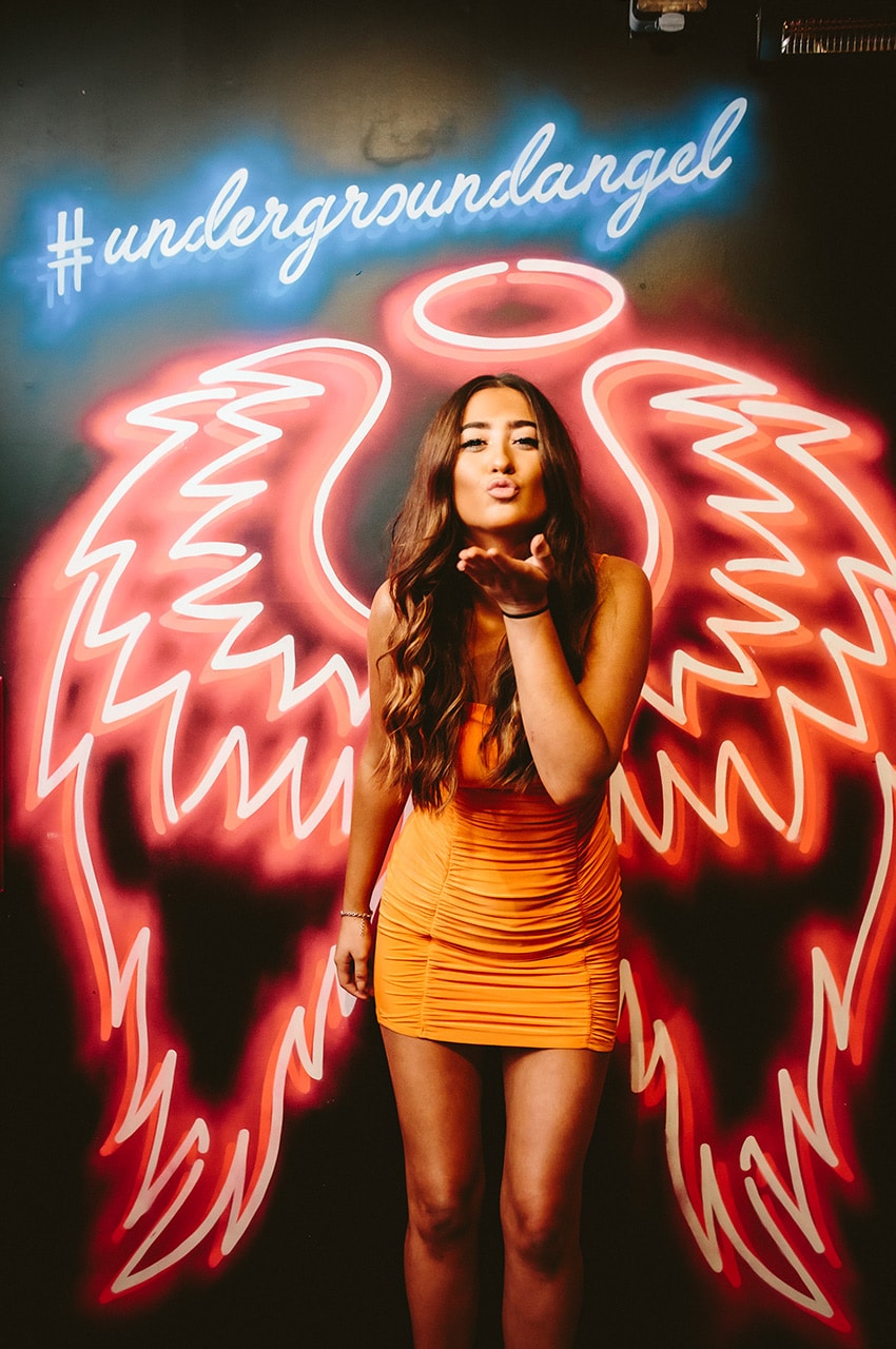 Girl in front of neon lights blowing a kiss